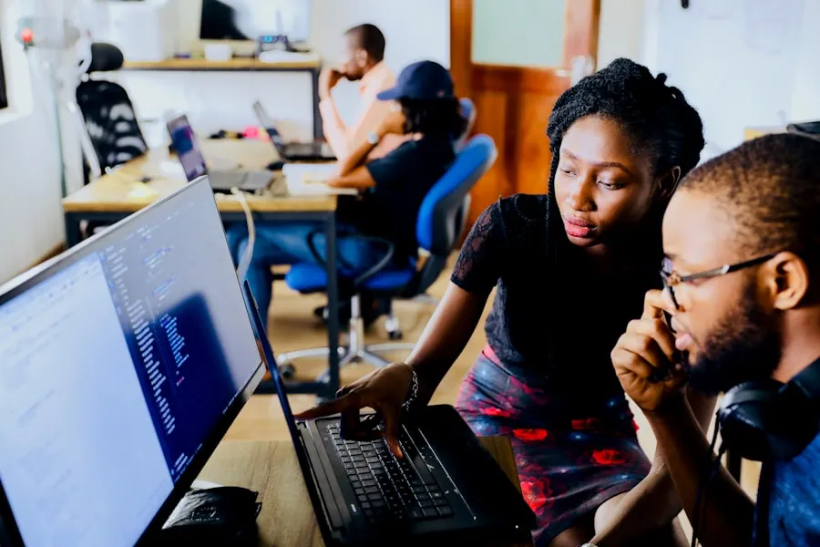 Two colleagues reviewing code together on a laptop in a shared workspace