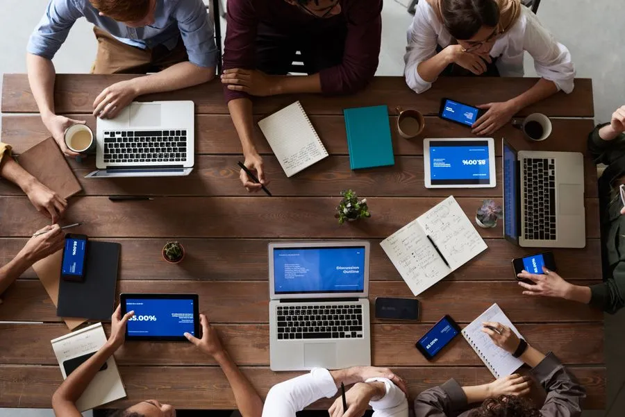 Overhead view of a team planning around a table of laptops, tablets, and notebooks