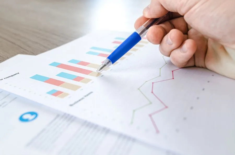 Hand pointing a pen at bar and line charts on a printed summary report